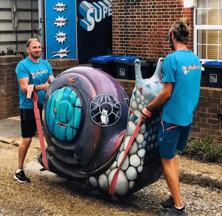 Two Supermover movers carrying a large decorated snail sculpture